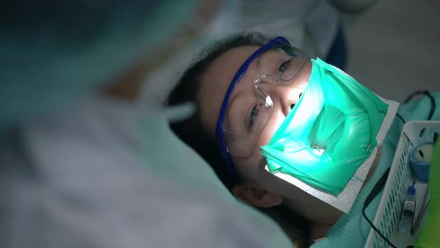 High angle view portrait of Caucasian woman in rubber dam on dental chair with doctor inserting root canal file in dental canal. Unrecognizable dentist doing procedure for patient in hospital indoors
