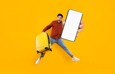 Excited Tourist Guy Jumping With Luggage And Showing Big Blank Smartphone