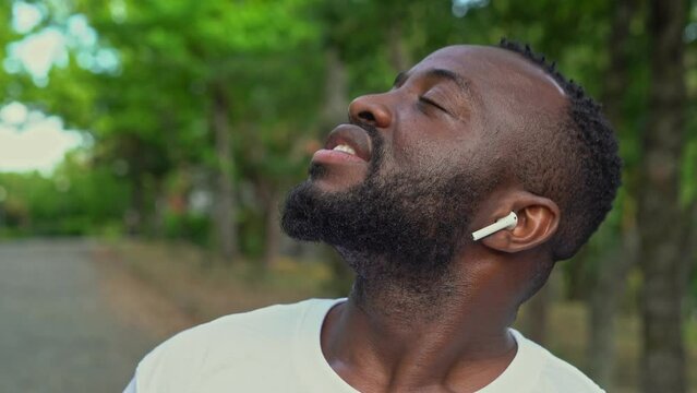 Close-up of a young african american man in the park listening music with airpods and closing his eyes