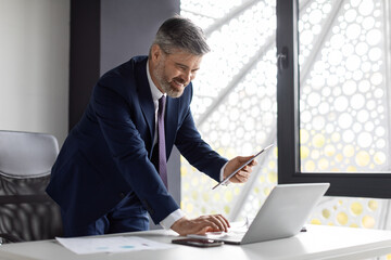 Technologies For Business. Middle Aged Businessman Using Digital Tablet And Laptop