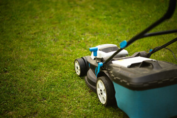 A lawn mower on wheels mows the green grass in the garden.Garden supplies. Grass mowing.