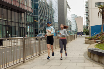 Two athletic women in sportswear are running around the city and listen music. Reaching the goal
