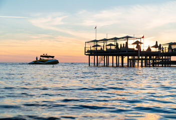 the boat sails on the sea past the pier with tourists at sunset. boat trips.