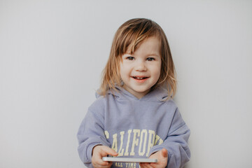 Little girl in violet hoodie using a phone on white background 