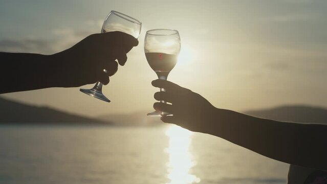 Slow motion video of a couple knocking over glasses of wine by the sea. Sunset, romantic evening of lovers near the ocean of rest.