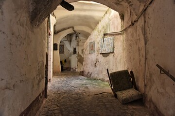Dirty, decrepit, algae green tunnel-like maze of alleys in Vietri sul Mare, Italy, incl. a broken chair, fragments of tiled wall murals and a clothes line in the back
