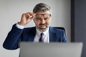 Frustrated Middle Aged Businessman Looking At Laptop Screen And Taking Off Glasses