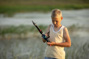 Little boy is fishing at sunset on the lake