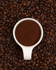 White porcelain cup of ground coffee between beans. Activity. Pleasant aroma. Start of the day. Good morning. Invigorating drink. Caffeine. Cheerfulness. Energetic product. Diversity