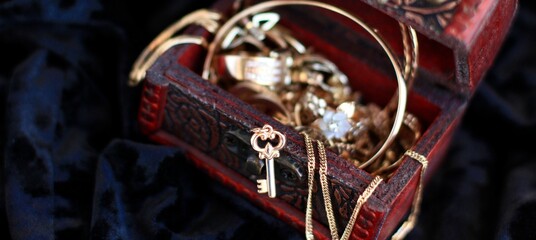 A golden key and vintage treasure chest full of jewelry such as rings, chains, pendants, earrings,...