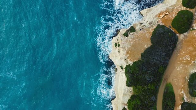 Pure blue Ocean water waves with light reflections crush mountain at Slow motion, Powerful storm on the sea Aerial top view