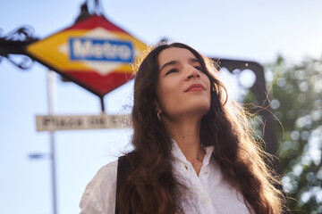 Portrait of a smiling young woman in front of Madrid metro station.