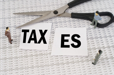 On financial reports, scissors, figurines of people and cut paper with the inscription - Taxes