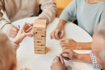 Close-up of unrecognizable seniors sitting at table and building toy towers from wooden blocks...