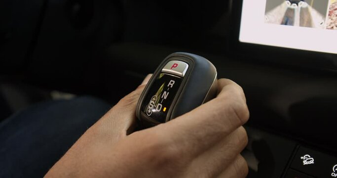 A Caucasian Man hand changes automatic gear selector from Reverse to Drive in a luxury off road suv in a sunny day under the forest