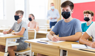 Portrait of teenager in protective face mask writing in workbook on lesson. New life reality during...