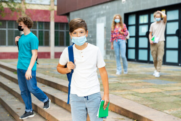 Teen boy in face mask with backpack going to home after finishing lessons at school on sunny day