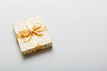 wrapped Christmas or other holiday handmade present in white paper with gold ribbon on colored background. Present box, decoration of gift on colored table, top view with copy space