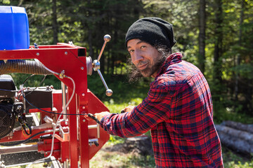 Portrait of a sawmill machine operative at work with black hair and stubble wearing a red checkered...
