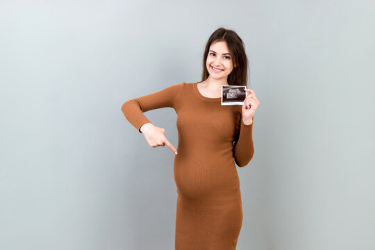 Cute Pregnant Lady Posing With Baby Sonography Photo Near Colored background. Concept of pregnancy, gynecology, medical test, maternal health