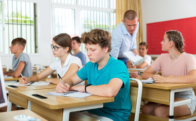 Group of teenage high school students diligently working in class, making notes of teacher lecture..