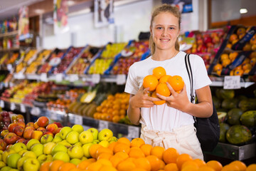 Pretty young european woman purchaser choosing juicy organic orange in a grocery store