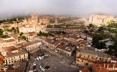 Aerial view of historic area of Trujillo overlooking central square surrounded by residential houses with medieval castle and Church of Santa Maria la Mayor in background in haze on spring day, Spain