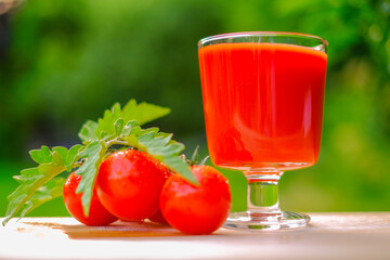 Tomato juice in a glass goblet and ripe tomatoes on a summer garden background.Vegetable natural juices. Red tomato organic juice