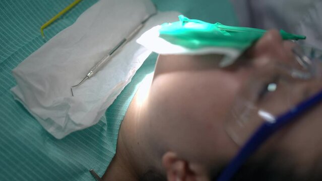 Close-up female hand placing dental explorer on napkin on client in dental chair. Unrecognizable Caucasian dentist curing tooth as assistant using curing light for filling polymerization. Slow motion