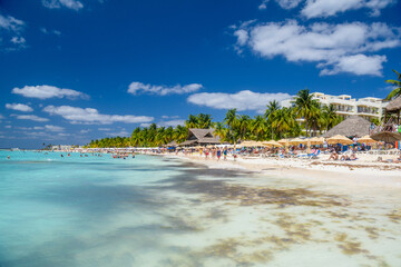 People swimming near white sand beach with umbrellas, bungalow bar and cocos palms, turquoise...