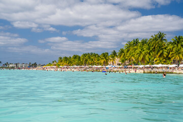 People swimming near white sand beach with umbrellas, bungalow bar and cocos palms, turquoise...