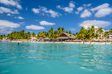 People swimming near white sand beach with umbrellas, bungalow bar and cocos palms, turquoise caribbean sea, Isla Mujeres island, Caribbean Sea, Cancun, Yucatan, Mexico