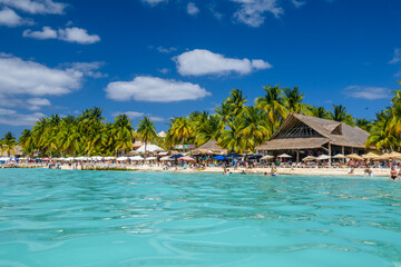 Fototapeta na wymiar People sunbathing on the white sand beach with umbrellas, bungalow bar and cocos palms, turquoise caribbean sea, Isla Mujeres island, Caribbean Sea, Cancun, Yucatan, Mexico