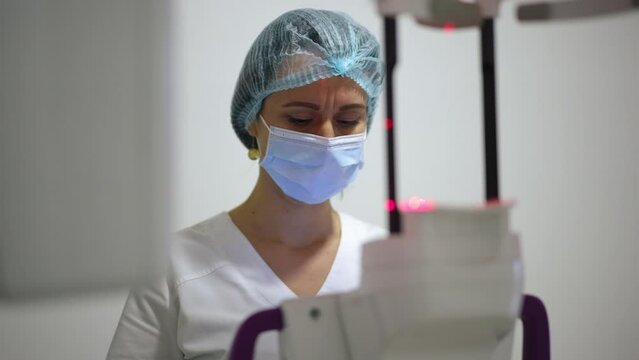 Portrait of focused beautiful doctor in face mask examining X-ray with cone beam scanner. Concentrated professional Caucasian dentist assistant analyzing dental image in hospital