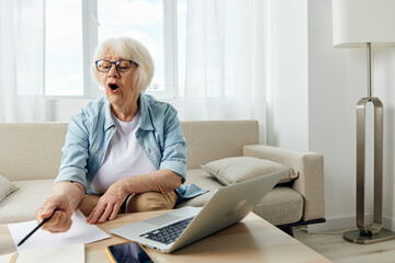 an elderly woman is passionate about the workflow, sitting at a coffee table on a cozy sofa at home and holding a training video conference, pointing with a pen to a sheet of paper with notes