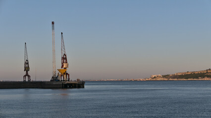 Fototapeta premium Cranes in Industrial harbor on the Tagus river in summer evening, Lisbon, Portugal