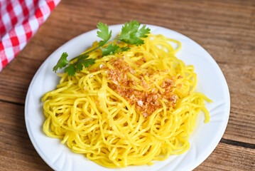 yellow noodles on white plate and wooden background , instant noodles yellow noodles rice vermicelli food with fried garlic and coriander