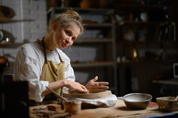 A ceramist makes a plate. Woman in an apron works in a pottery workshop. 