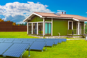 Solar panels on summer lawn. Renewable modules. Power plant. Solar panels in cottage village. Eco energy supply. Solar power supply panels. Eco-friendly Sun source electricity. Wooden houses - obrazy, fototapety, plakaty