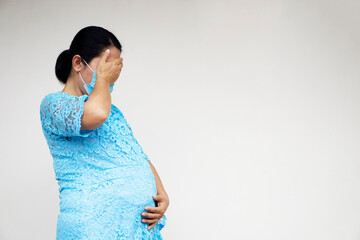 Pregnant Asian woman wears hygienic face mask, holds her big belly, sad and cry. Concept :...