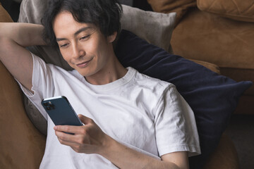 ソファーに寝転んでリラックスしながら携帯電話を見ている男性