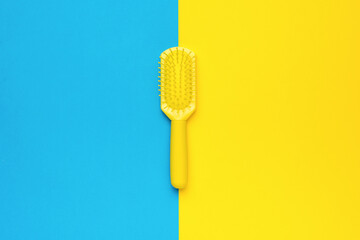 Yellow comb on a bright yellow and blue background. Minimal hair care concept.