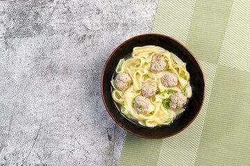 Noodle Meatball Soup in a a bowl on a dark grey background. Top view, flat lay