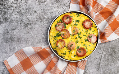 Omelet with herbs and sausage on a round plate on a dark grey background. Top view, flat lay