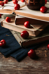 Atmospheric photo of ripe red sweet cherries and books on the rustic wooden background. Selective focus. Shallow depth of field.