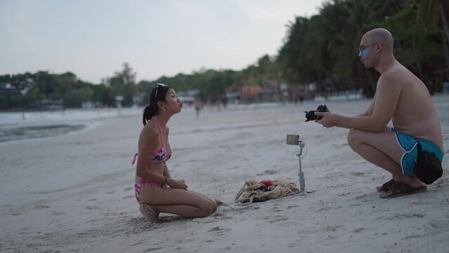 Caucasian photographer man take pictures of Thai girl in a bikini on a beach