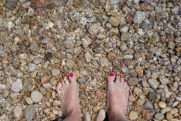 Female feet on the pebble beach, top view. Summer pedicure