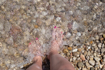 Female feet on the pebble beach, top view. Summer pedicure