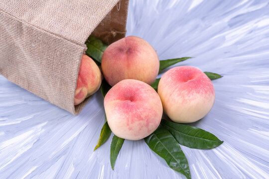 Fresh Sweet Peach on blue wooden  background, Pink and yellow Peach fruit with leaf with natural color cloth bagt.