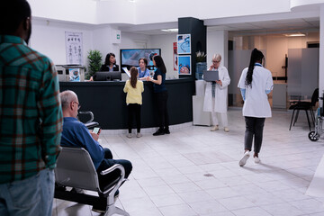 Hospital front desk reception with mother and child filling form for doctor appointment in private practice clinic. Diverse people waiting in busy healthcare facility for medical consultation.